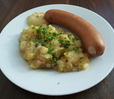 Warmer Kartoffelsalat mit Speck und Bockwurst, verfeinert mit Schnittlauch und Worcestersoße
